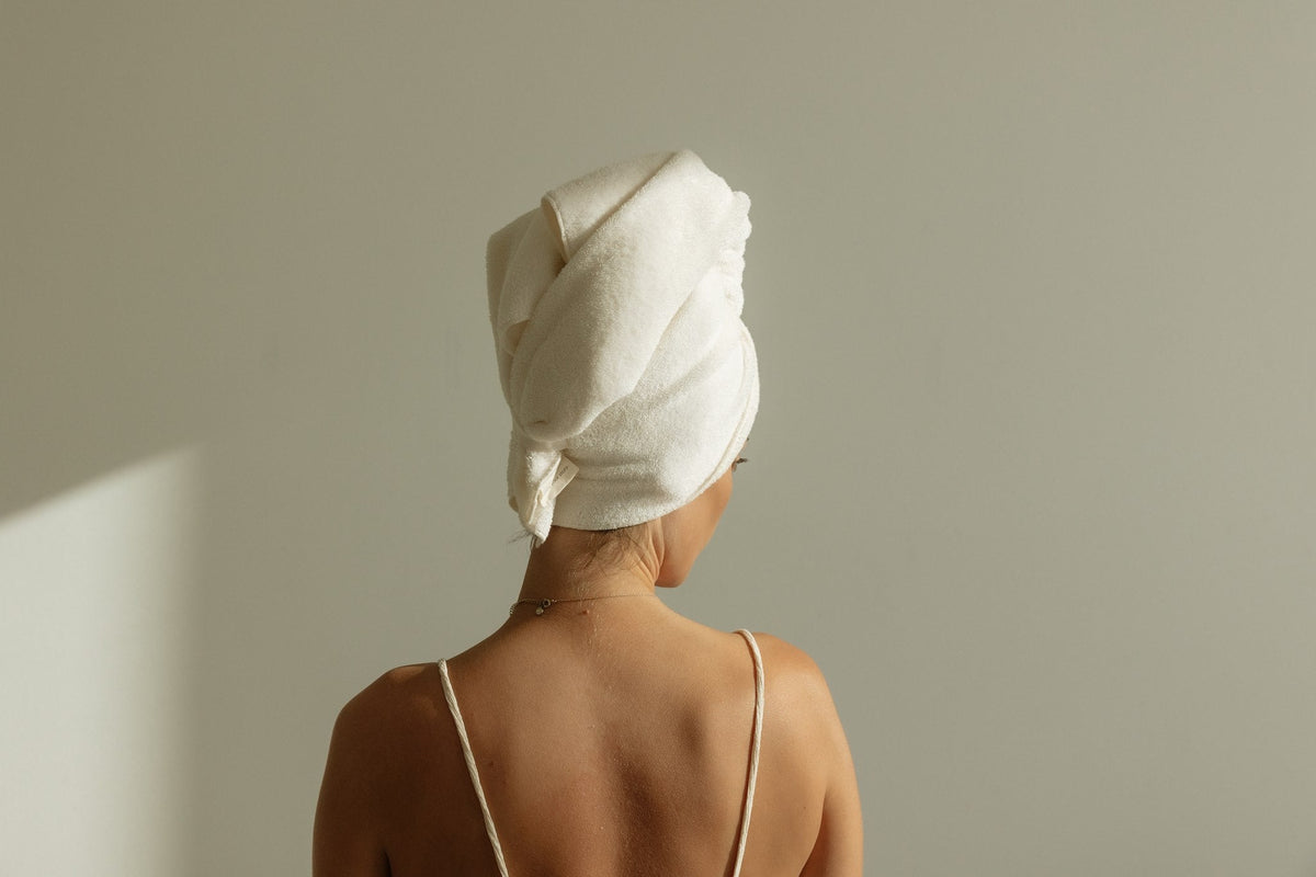 Woman from behind wearing a COTI knitted cotton terry hair towel wrapped and tucked at the back