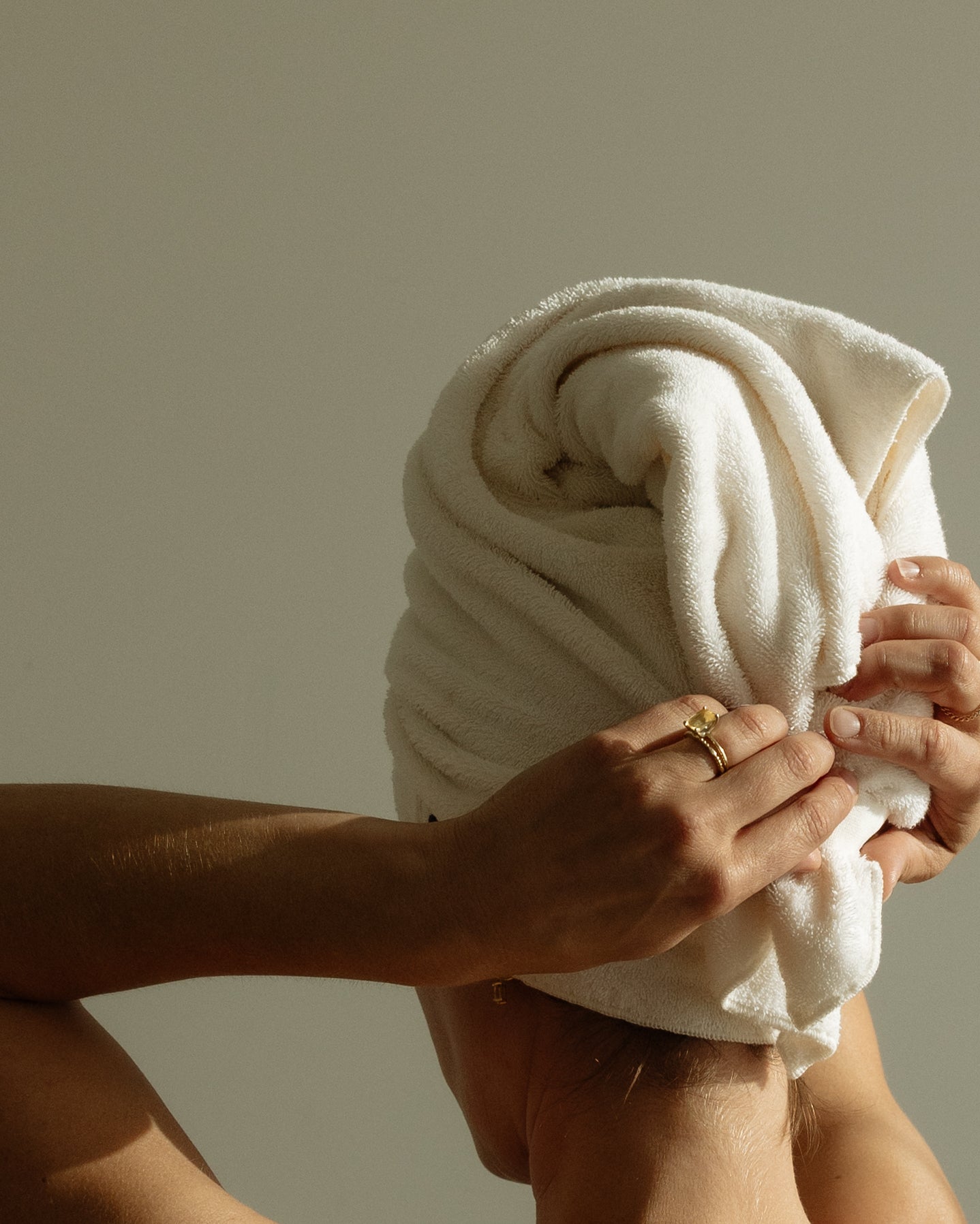 Woman with long wet hair wrapped in a cream COTI hair towel that stays on without slipping.
