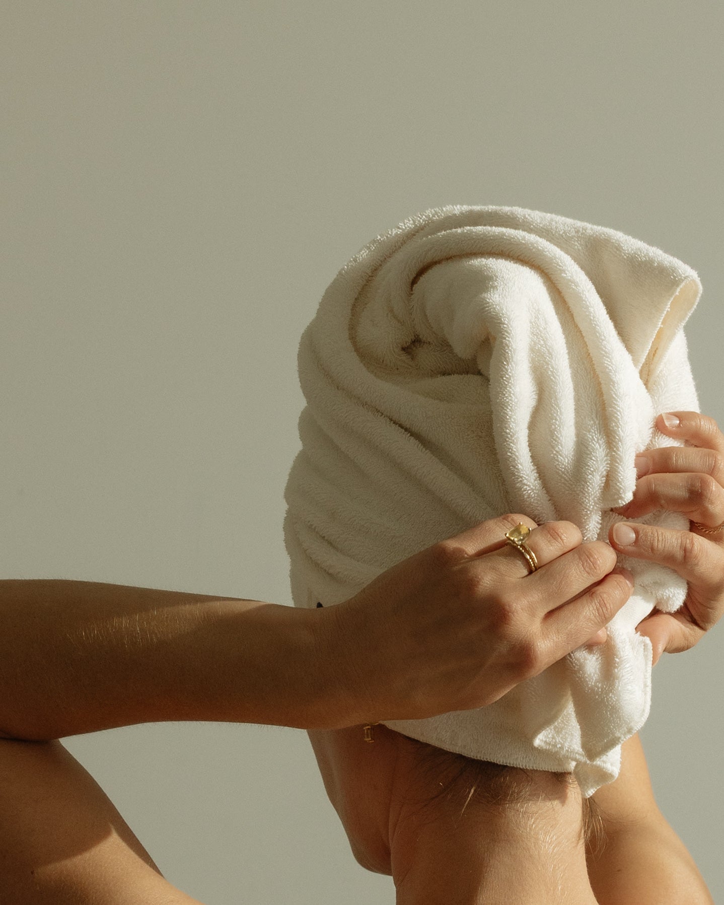 Hands wrapping a cream COTI hair towel.