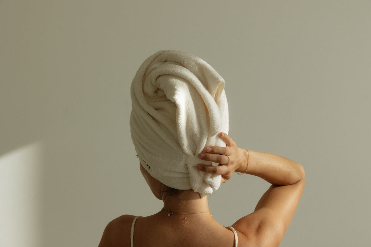 Woman seen from behind wearing a COTI knitted cotton terry hair towel wrapped and tucked in place.