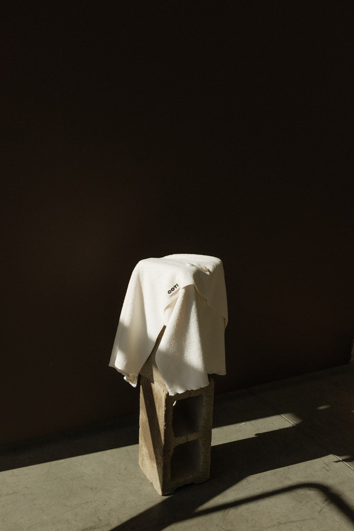 The COTI hair towel draped over a block in a sunlight streaming through with a dark background.