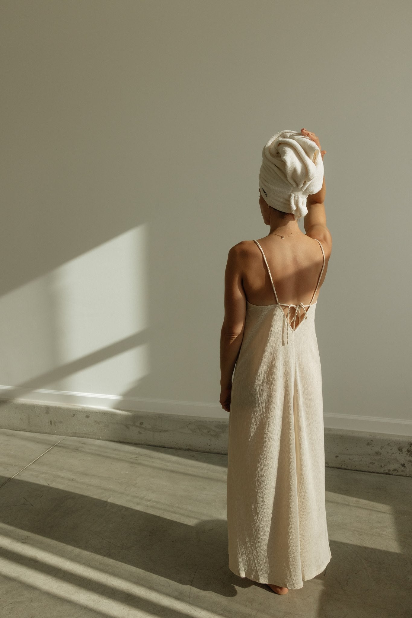 Woman in a cream slip dress with a COTI hair towel wrapped on her head.