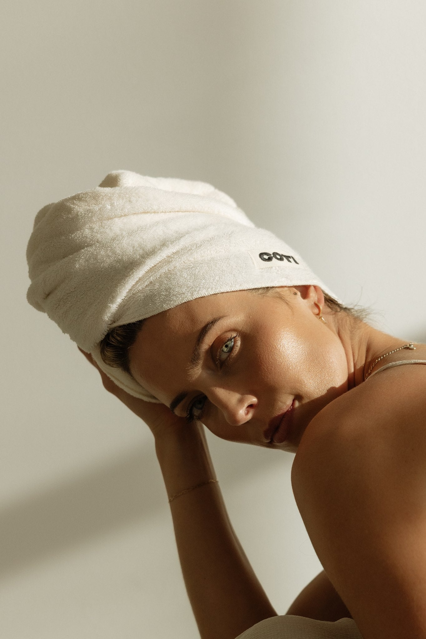 Woman resting her head, hair wrapped in a cream COTI hair towel.